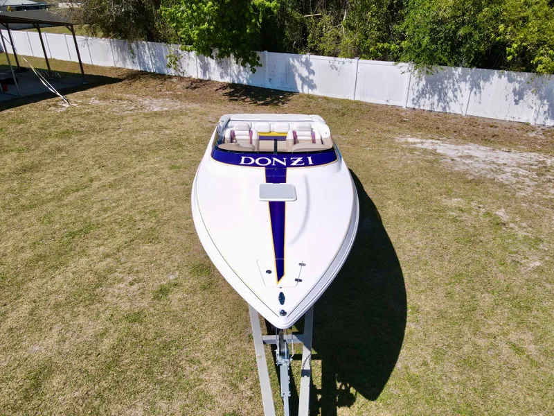 Slide: The Image of 1999 Donzi 26 ZX boat on trailer, parked on grass, surrounded by trees and fence. - 6