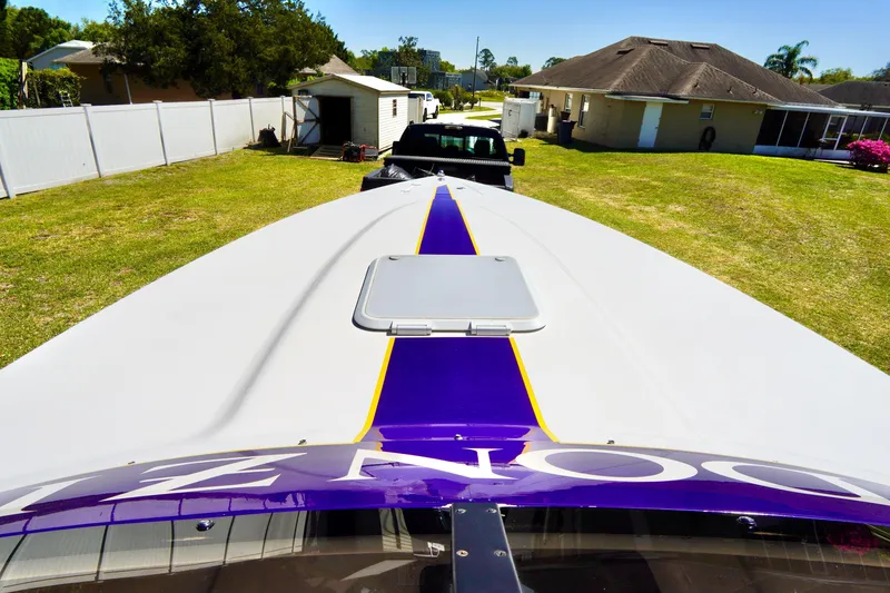 Slide: The Image of 1999 Donzi 26 ZX boat with purple stripe, parked on grass, view from bow. - 8