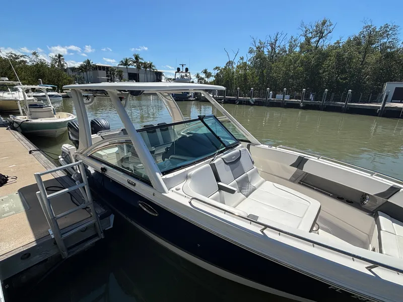 Slide: The Image of 2021 Chaparral 300 OSX boat docked on a sunny day, surrounded by trees and water. - 2