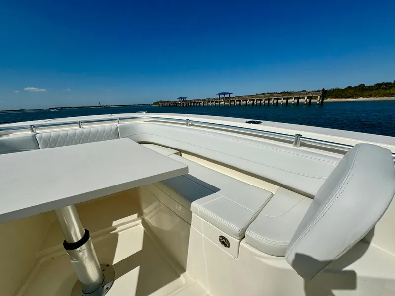 Slide: The Image of 2020 Cobia 350 Center Console boat interior with seating and table, near a scenic pier. - 26