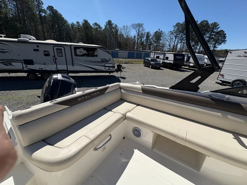 Slide: The Image of 2019 Bayliner 210 Deck Boat interior with beige seating, parked near RVs and trailers. - 10