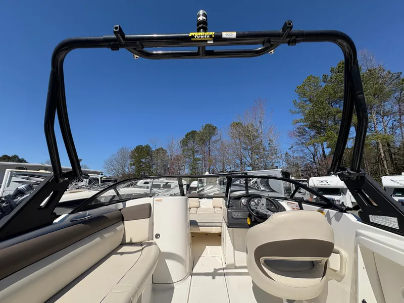 Slide: The Image of 2019 Bayliner 210 Deck Boat interior with seating and steering wheel, under clear blue sky. - 13