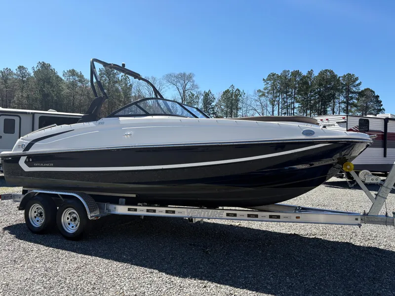 Slide: The Image of 2019 Bayliner 210 Deck Boat on trailer, parked outdoors under clear blue sky. - 4