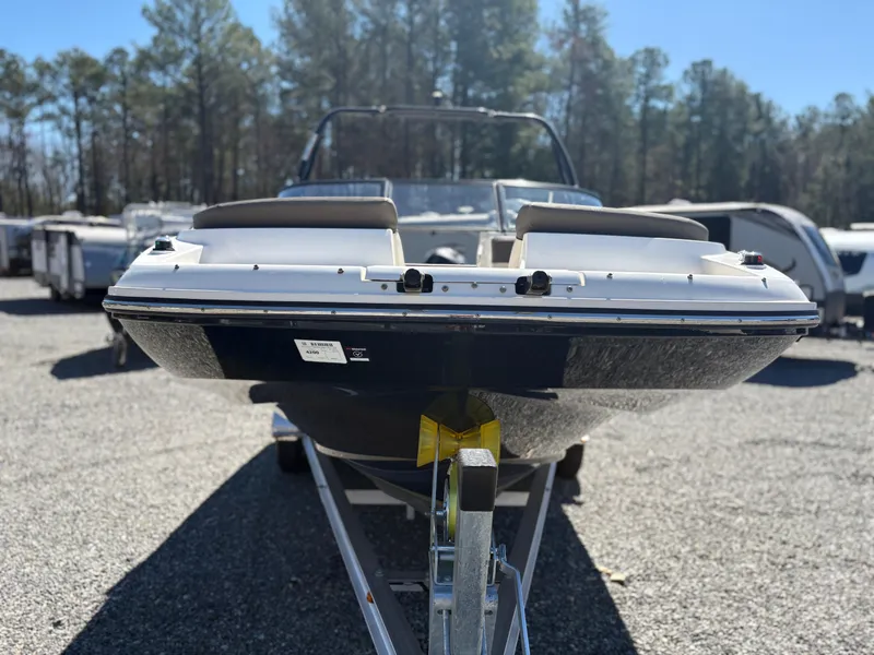 Slide: The Image of 2019 Bayliner 210 Deck Boat on trailer, parked outdoors with trees in background. - 5