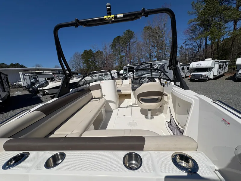 Slide: The Image of 2019 Bayliner 210 Deck Boat interior with seating and cup holders, parked outdoors. - 7