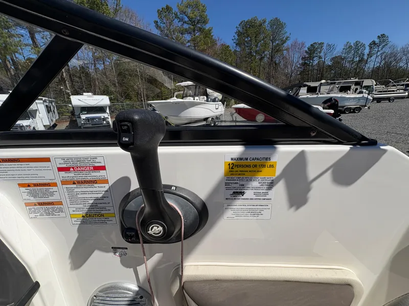 Slide: The Image of 2019 Bayliner 210 Deck Boat control panel with capacity warning, parked in a lot with trees. - 8