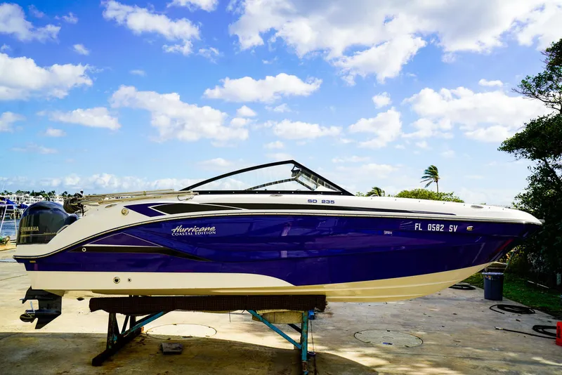 Slide: The Image of 2021 Hurricane SunDeck 235 OB boat on stand, blue and white design, clear sky background. - 0