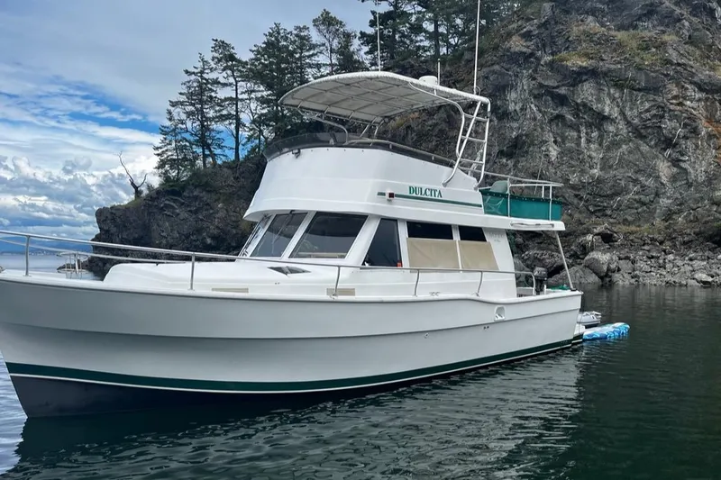 Slide: The Image of 1997 Mainship 350 yacht anchored near rocky shoreline with trees. - 0