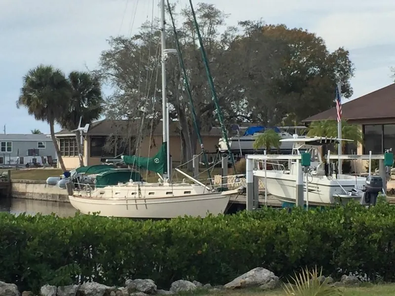Slide: The Image of 1998 Island Packet 40 sailboat docked near a house with trees and greenery. - 1
