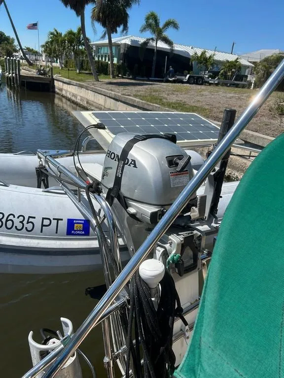 Slide: The Image of 1998 Island Packet 40 sailboat with Honda outboard motor and solar panel, docked by palm trees. - 17