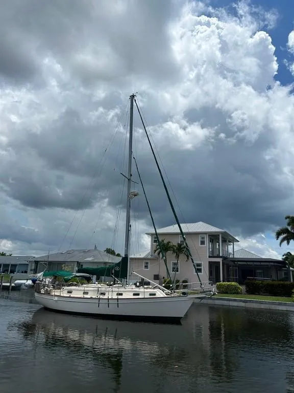 Slide: The Image of 1998 Island Packet 40 sailboat docked by waterfront homes under cloudy sky. - 2