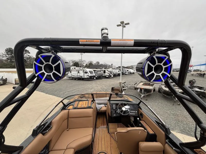 Slide: The Image of 2025 Moomba Max boat interior with speakers, brown seating, and dashboard, parked near RVs. - 11