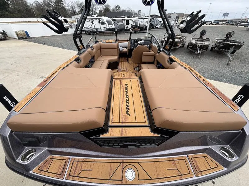 Slide: The Image of 2025 Moomba Max boat interior with tan seating and wood accents, parked outdoors. - 9