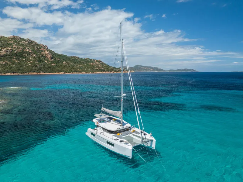 Slide: The Image of 2025 Lagoon 38 catamaran sailing in clear turquoise waters near a rocky coastline. - 5