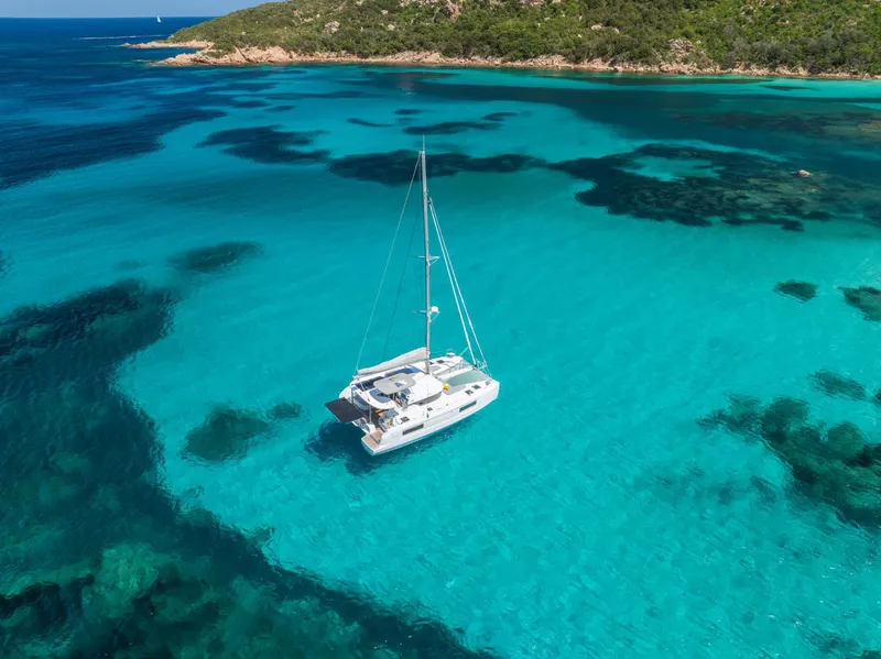 Slide: The Image of 2025 Lagoon 38 catamaran sailing in clear turquoise waters near a lush coastline. - 66