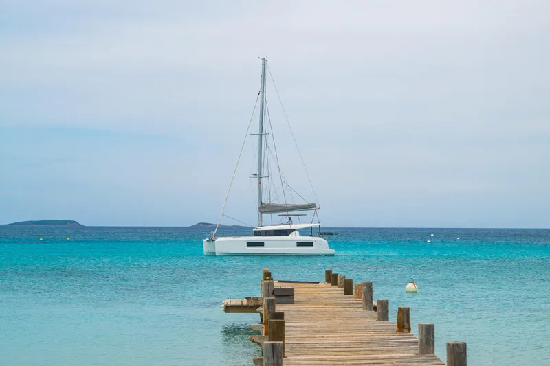 Slide: The Image of 2025 Lagoon 38 catamaran anchored near a wooden pier in clear blue waters. - 75