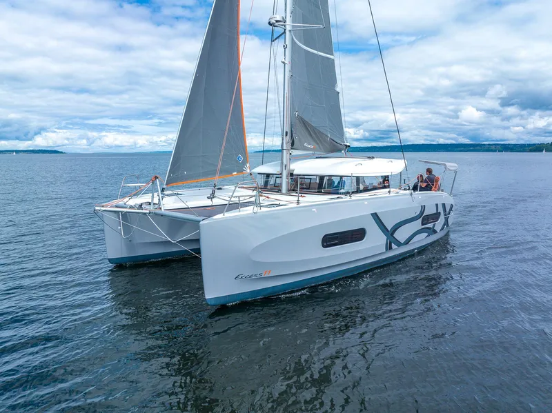 The Image of 2025 Excess 11 catamaran sailing on calm waters under a cloudy sky. - 0