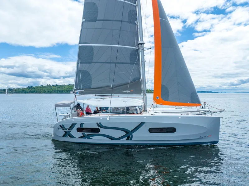 Slide: The Image of 2025 Excess 11 catamaran sailing on a calm lake under a partly cloudy sky. - 2