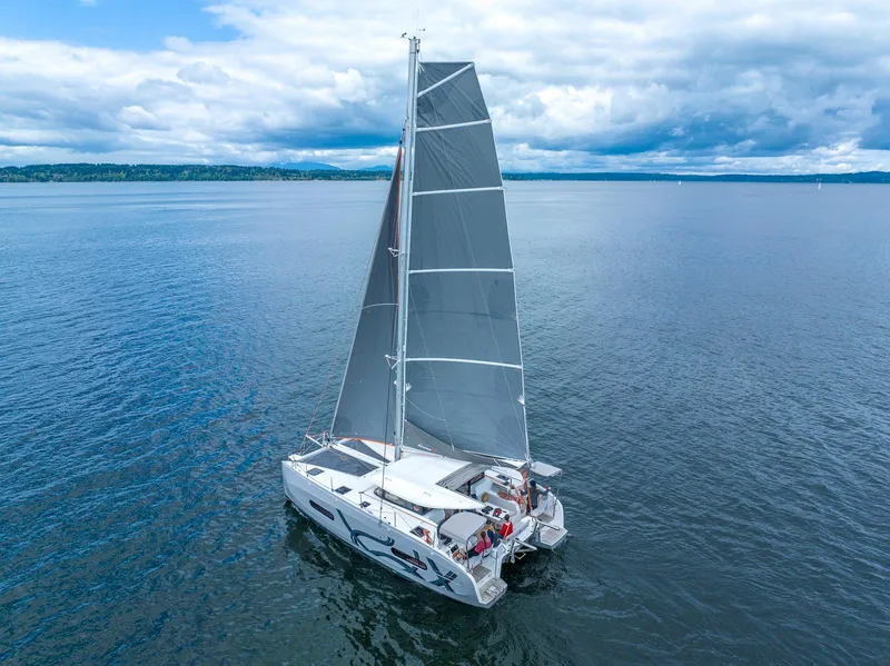 Slide: The Image of 2025 Excess 11 catamaran sailing on calm blue waters under a cloudy sky. - 6