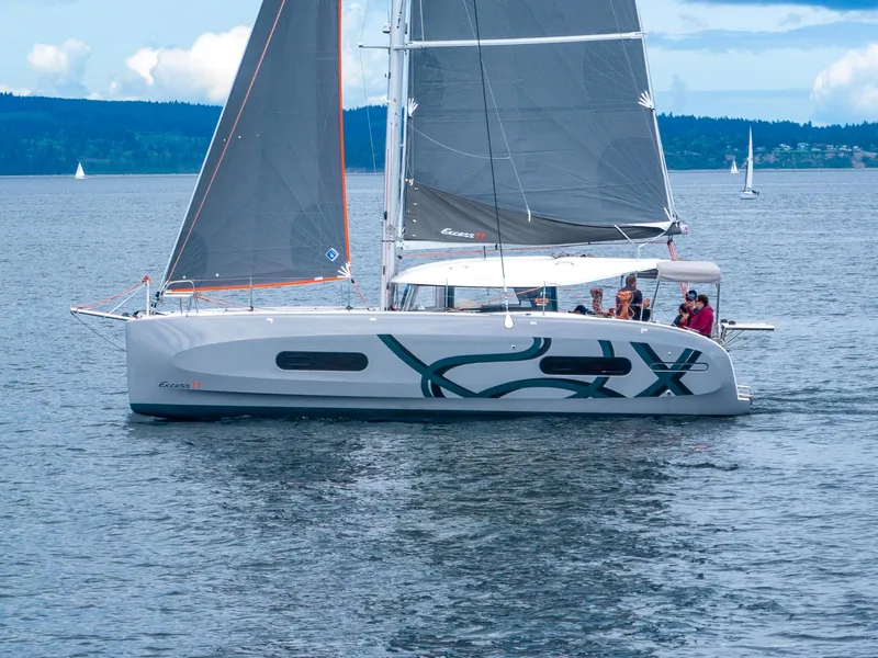 Slide: The Image of 2025 Excess 11 sailboat cruising on a calm lake with scenic background. - 1