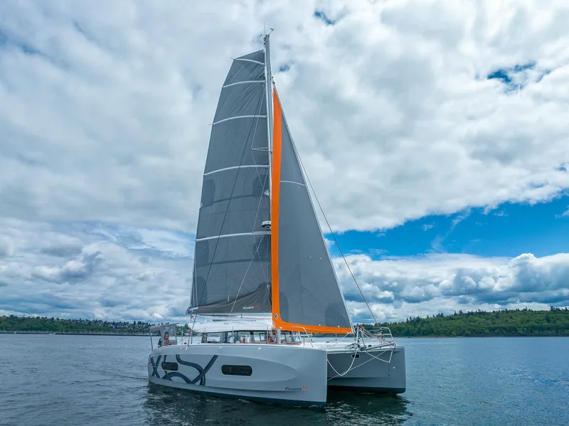 Slide: The Image of 2025 Excess 11 catamaran sailing on a calm lake under a cloudy sky. - 7