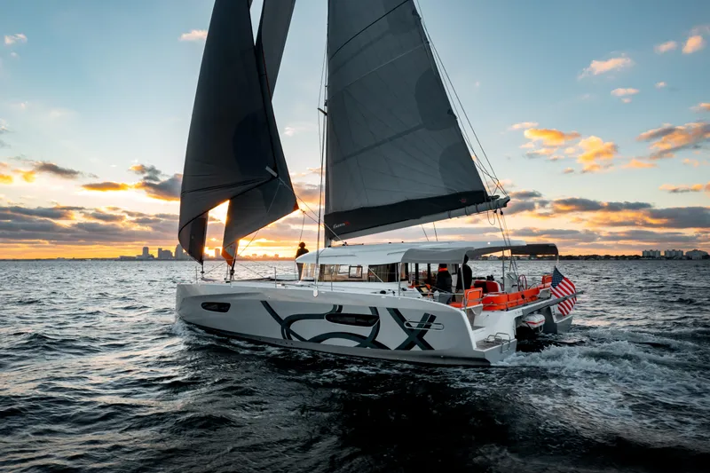 Slide: The Image of Sailing yacht Excess 14, 2025 model, cruising at sunset with city skyline in background. - 1