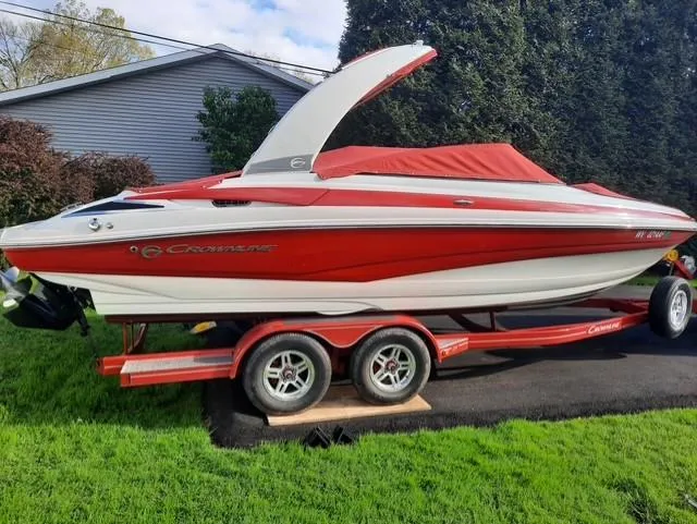The Image of 2015 Crownline 235 SS boat with red cover on a trailer, parked on grass. - 1