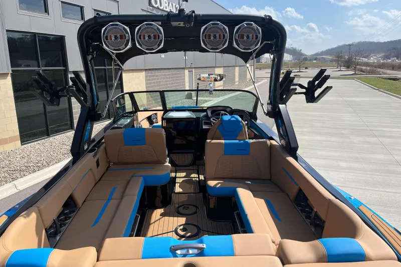 Slide: The Image of 2022 MasterCraft X26 boat interior with tan and blue seating, tower speakers, and wakeboard racks. - 10