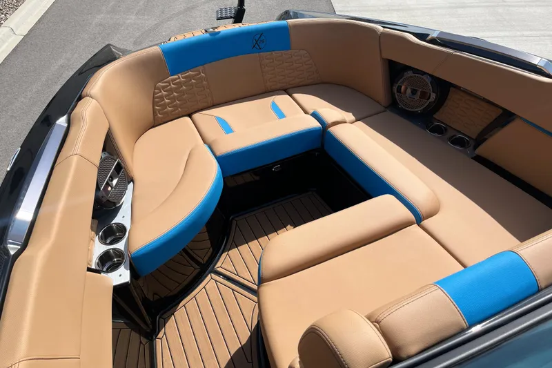Slide: The Image of 2022 MasterCraft X26 boat interior with tan and blue seating, featuring cup holders and speakers. - 13