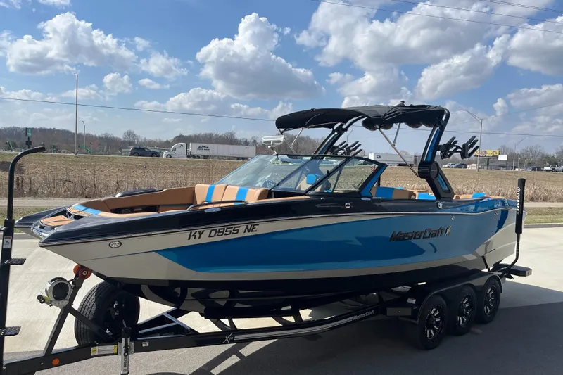 Slide: The Image of 2022 MasterCraft X26 boat on trailer, blue and white, parked outdoors under a cloudy sky. - 5