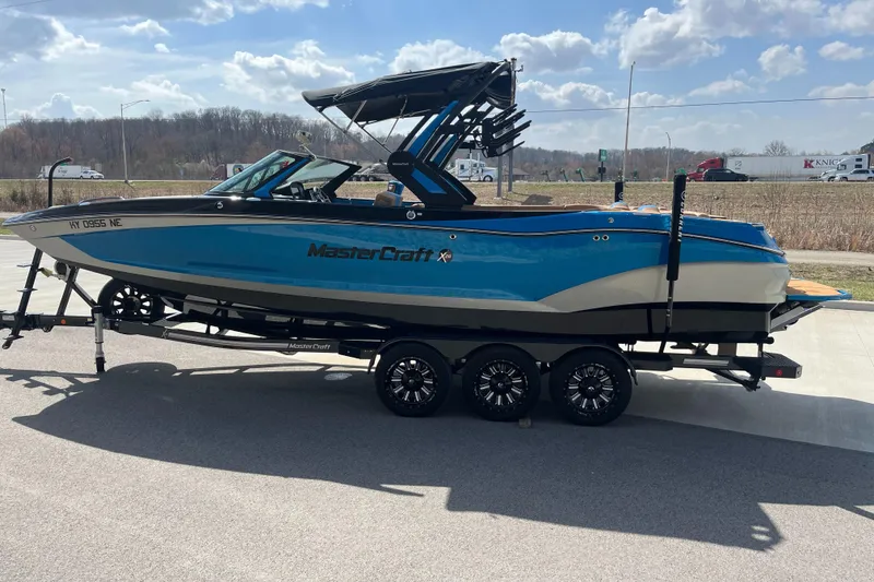 Slide: The Image of 2022 MasterCraft X26 boat on trailer, blue and white, parked outdoors under cloudy sky. - 6