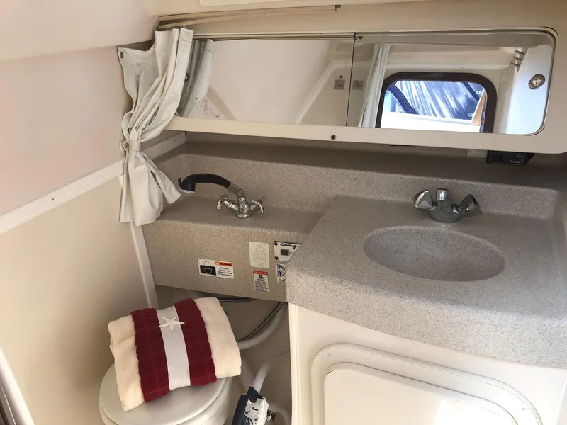 Slide: The Image of 2005 Catalina 310 bathroom with sink, mirror, and toilet, featuring a red-striped towel. - 10