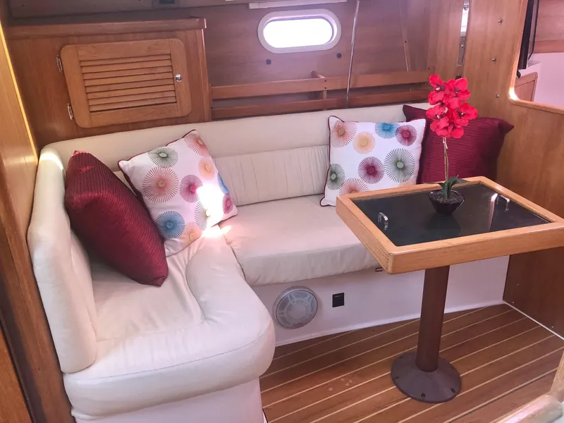 Slide: The Image of Cozy Catalina 310 yacht interior with cushioned seating, decorative pillows, and a small table, 2005 model. - 5
