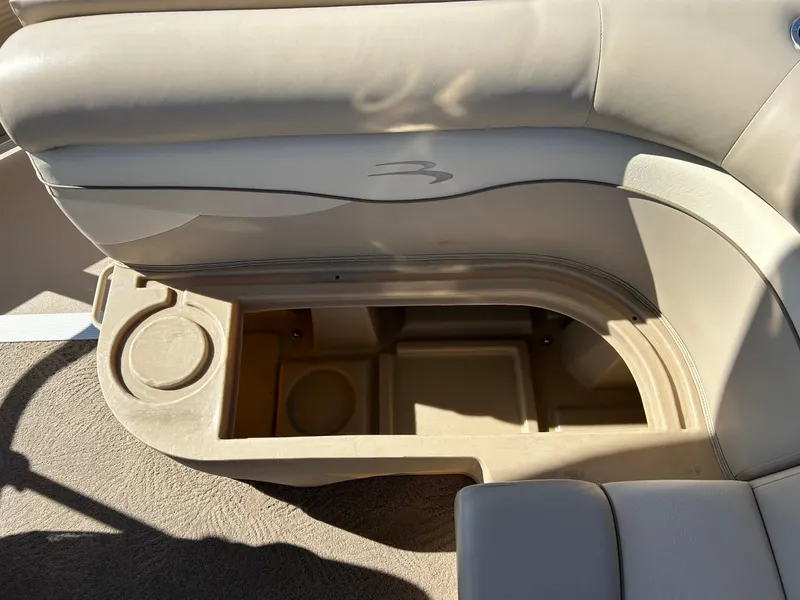 Slide: The Image of 2012 Bennington 20SLi boat seat storage compartment with beige upholstery and cup holder. - 20