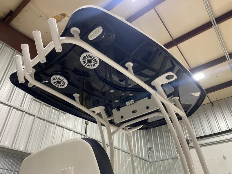 Slide: The Image of 2022 Tidewater 2500 Carolina Bay boat's T-top with rod holders and speakers in a metal building. - 10