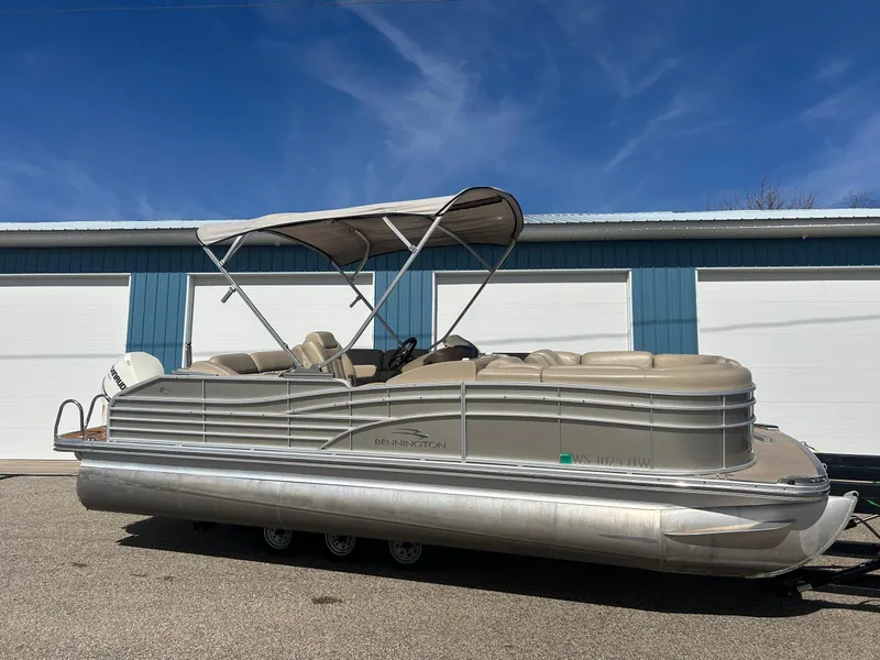 Slide: The Image of 2012 Bennington 2250RCL pontoon boat with canopy, parked outdoors against blue and white building. - 2