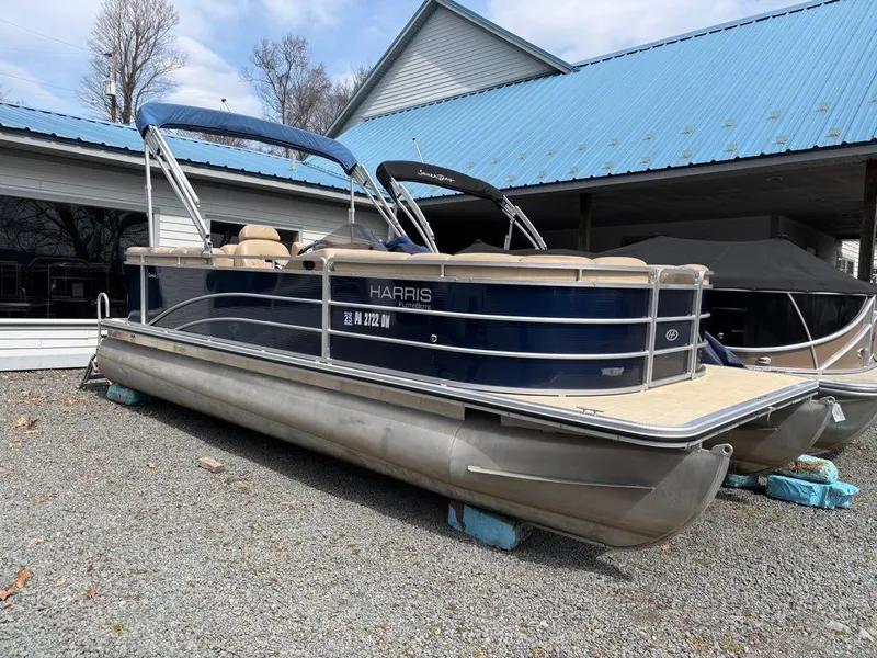 Slide: The Image of 2014 Harris Cruiser 220 pontoon boat with blue canopy, parked on gravel. - 6