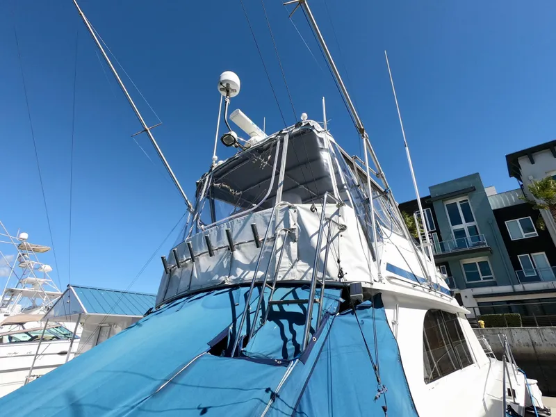 Slide: The Image of 1986 Bertram 46 Sportfisher boat with blue cover and antennas, docked under clear sky. - 10