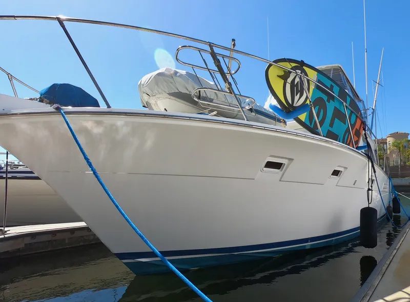 Slide: The Image of 1986 Bertram 46 Sportfisher yacht docked, featuring sleek design and vibrant surfboard on deck. - 2