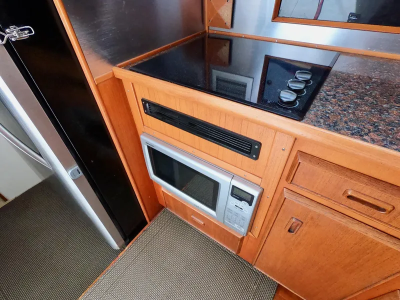 Slide: The Image of 1986 Bertram 46 Sportfisher kitchen with stove, microwave, and wooden cabinetry. - 26