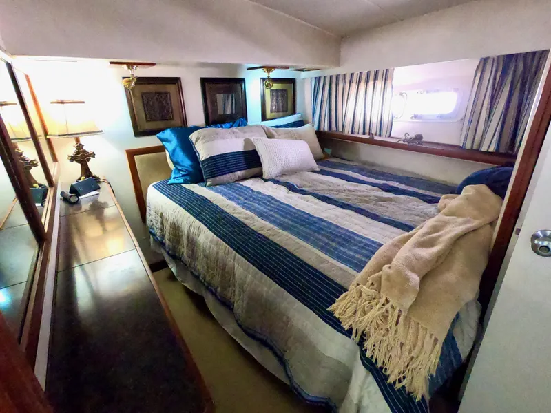 Slide: The Image of 1986 Bertram 46 Sportfisher cabin with cozy bed, striped bedding, and nautical decor. - 29