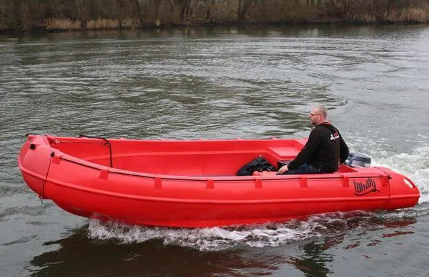 Slide: The Image of Red 2025 Whaly 500R Pro boat navigating a calm river with a person onboard. - 7