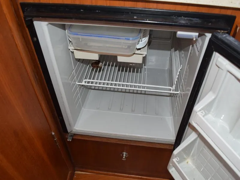 Slide: The Image of Open refrigerator inside 2006 Tiara Yachts 3200 Open, featuring empty shelves and wooden cabinetry. - 47