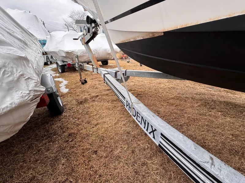 Slide: The Image of Boat trailer labeled "Phoenix" under a covered Mako 191, 1997 model, on dry grass. - 4