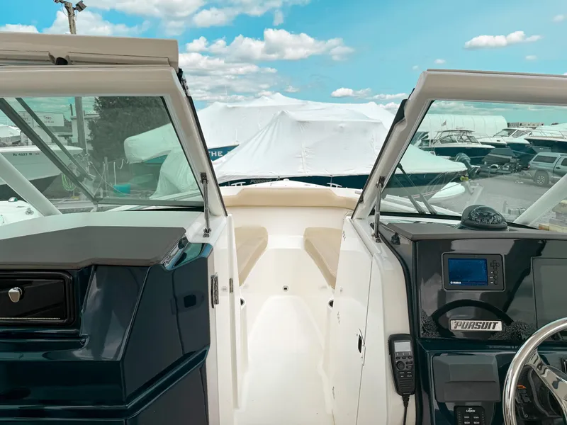 Slide: The Image of 2020 Pursuit DC 266 Dual Console boat interior with dashboard and seating, under a blue sky. - 14