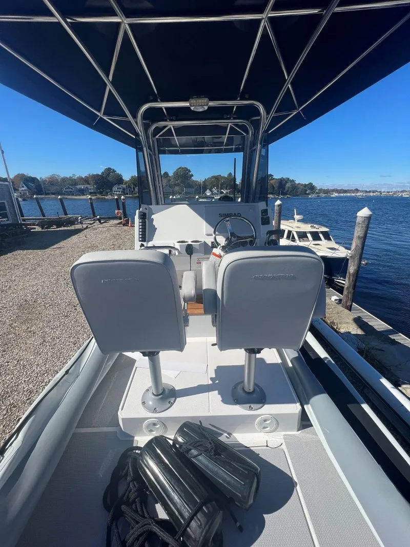 Slide: The Image of 2023 Protector 250 Chase boat interior with dual seats, docked by a scenic waterfront. - 4