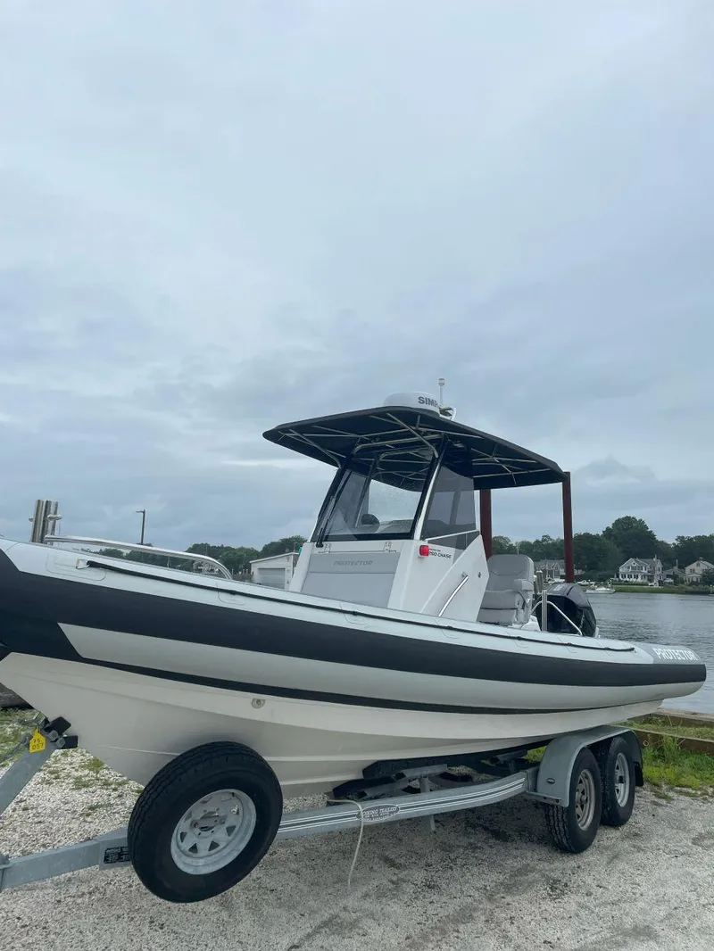 Slide: The Image of 2023 Protector 250 Chase boat on trailer by waterfront, overcast sky. - 6