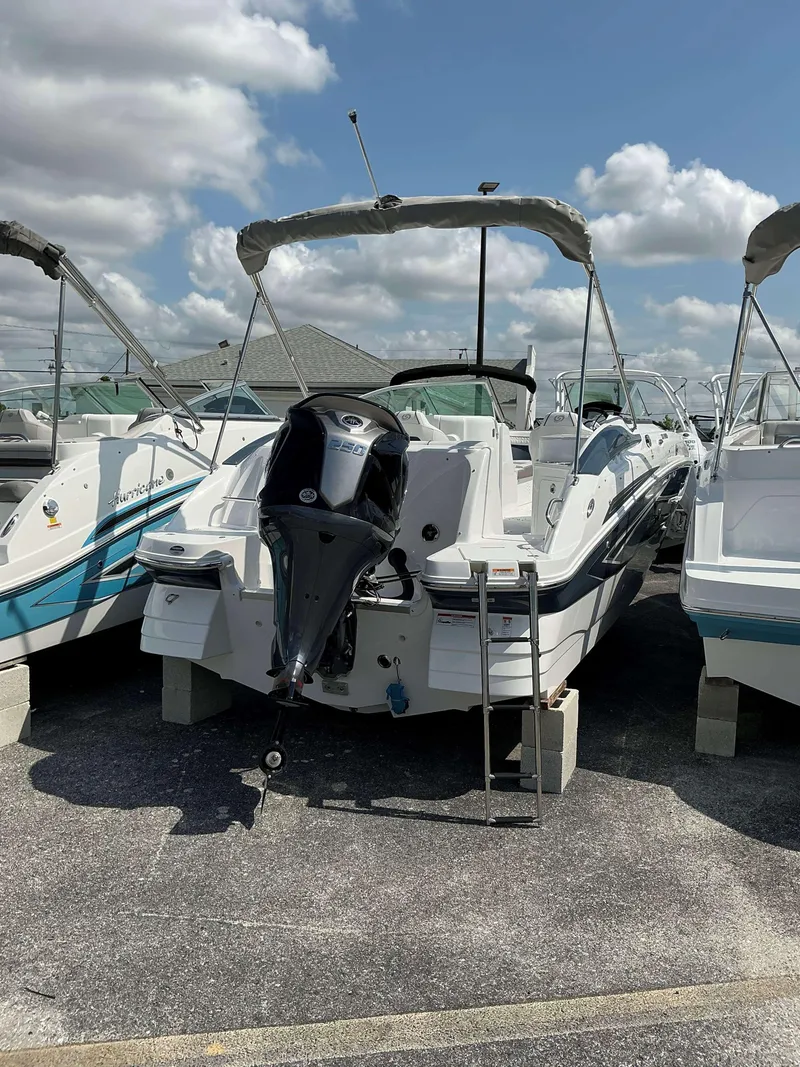 Slide: The Image of 2025 Hurricane 2400 SD boat with outboard motor, parked on blocks under a cloudy sky. - 3