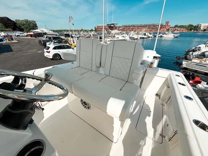Slide: The Image of 2025 Pursuit S 268 Sport boat with white seating, docked near waterfront and parked cars. - 14