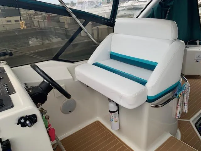 Slide: The Image of 1994 Silverton 34 Express boat cockpit with white and teal seating, steering wheel, and fire extinguisher. - 13